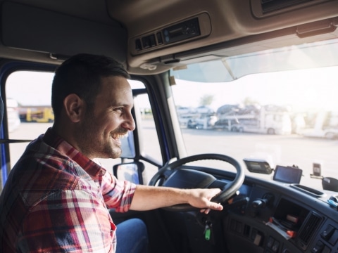 Professional middle aged truck driver in casual clothes driving truck vehicle going for a long transportation route.